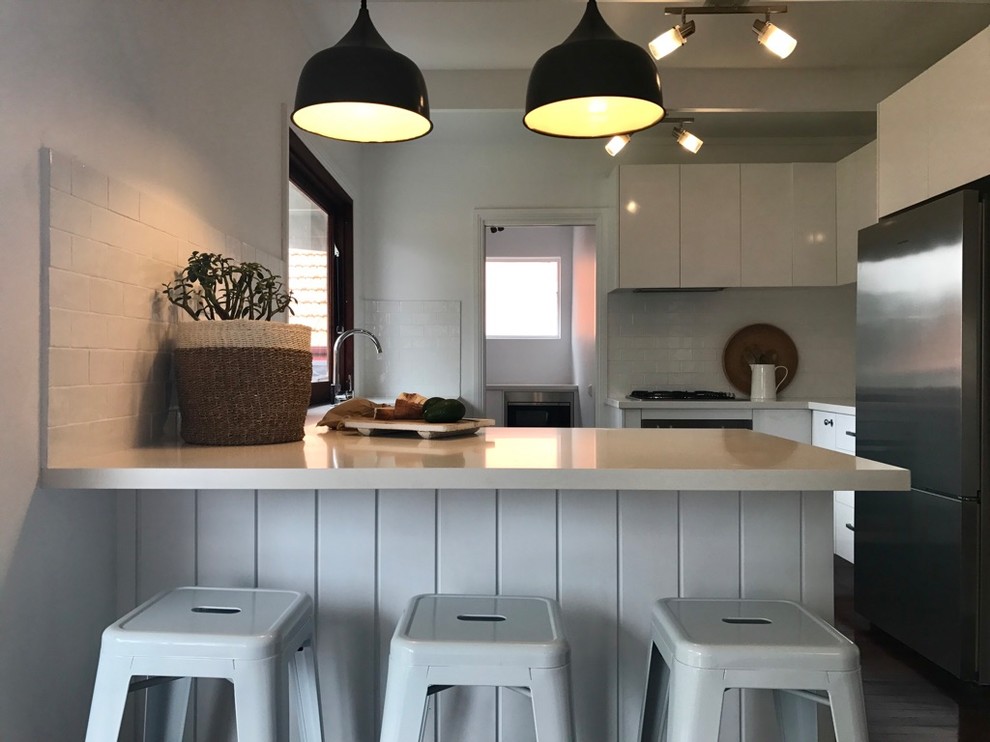 Inspiration for a small beach style l-shaped separate kitchen in Sydney with white cabinets, quartz benchtops, white splashback, with island, white benchtop, a double-bowl sink, ceramic splashback, stainless steel appliances, painted wood floors and brown floor.