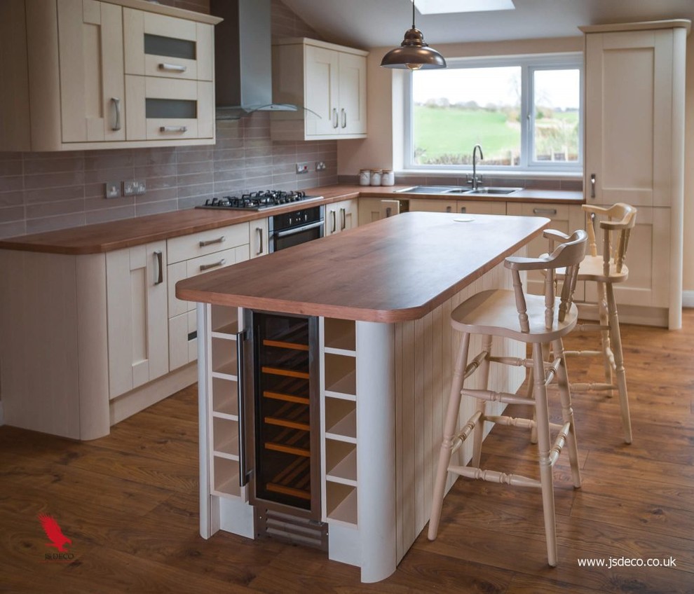 This is an example of a large country l-shaped open plan kitchen in Other with a triple-bowl sink, shaker cabinets, beige cabinets, laminate benchtops, grey splashback, porcelain splashback, panelled appliances, laminate floors, with island and multi-coloured floor.