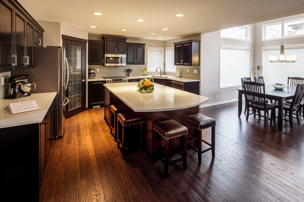 Inspiration for a large transitional u-shaped dark wood floor and brown floor eat-in kitchen remodel in Calgary with a double-bowl sink, raised-panel cabinets, dark wood cabinets, quartz countertops, gray backsplash, ceramic backsplash, stainless steel appliances and an island