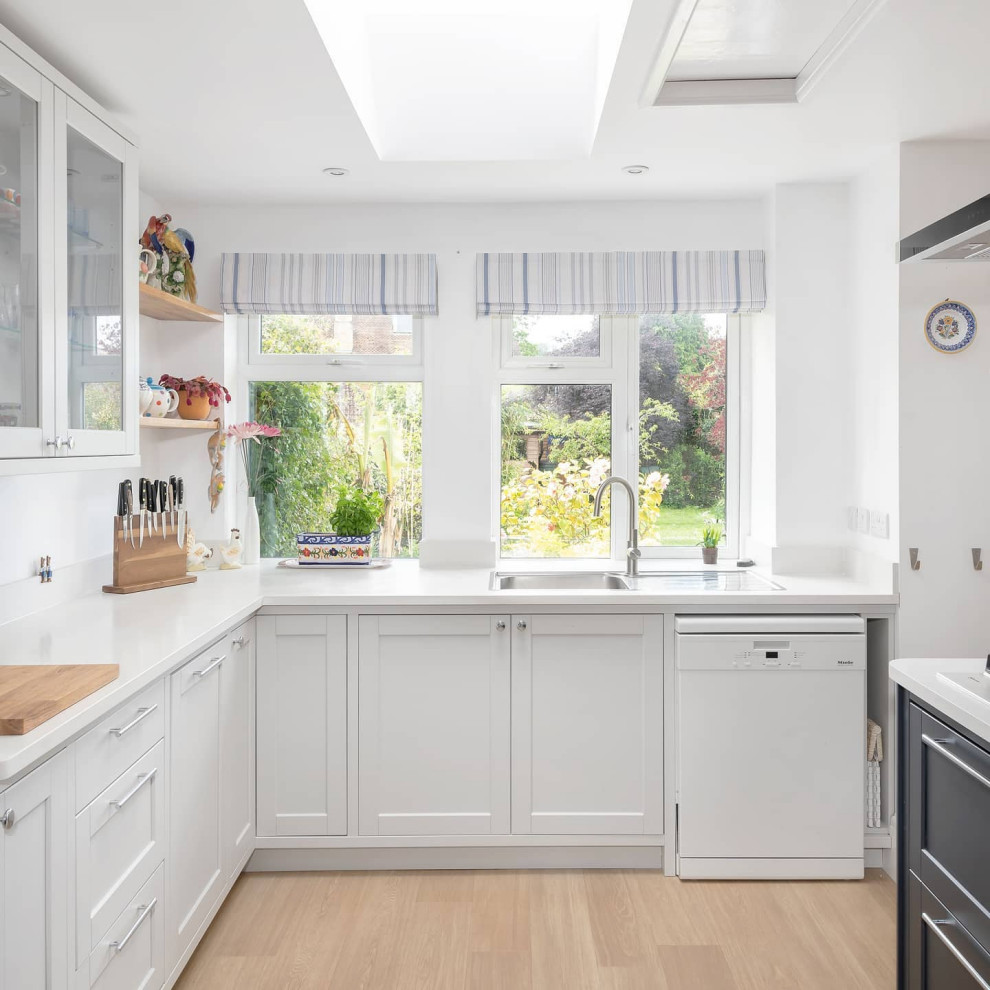Photo of a large classic u-shaped kitchen/diner in Other with shaker cabinets, white cabinets, light hardwood flooring, beige floors, white worktops, a double-bowl sink, composite countertops, white splashback, engineered quartz splashback, white appliances and an island.
