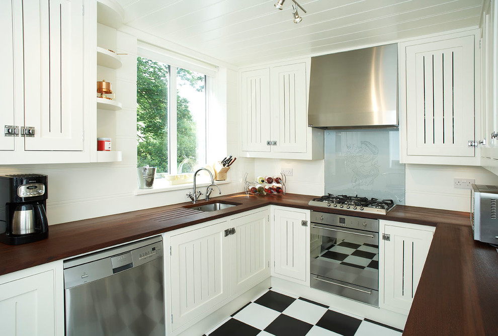 Inspiration for a traditional u-shaped kitchen in Oxfordshire with an undermount sink, white cabinets, grey splashback, glass sheet splashback, stainless steel appliances and wood benchtops.