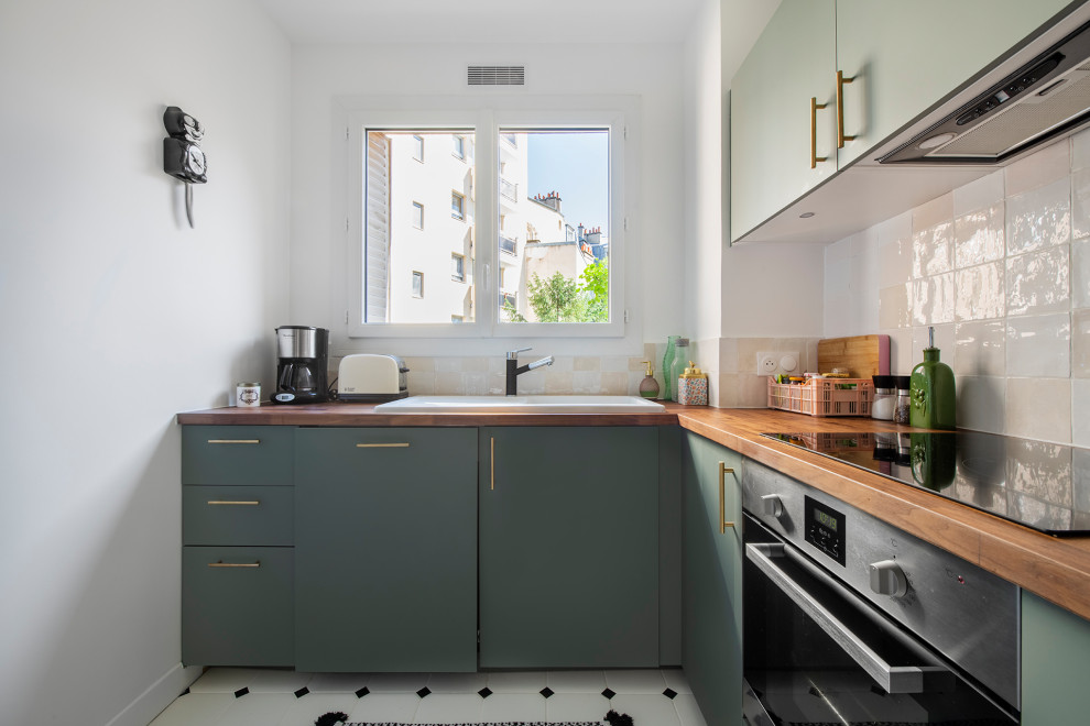 Photo of a small modern l-shaped separate kitchen in Paris with a drop-in sink, flat-panel cabinets, green cabinets, wood benchtops, white splashback, terra-cotta splashback, black appliances, porcelain floors, no island, white floor and brown benchtop.