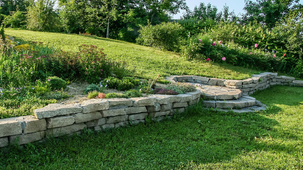 Inspiration for a traditional garden with a retaining wall and natural stone pavers.
