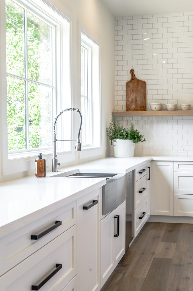 Inspiration for a large transitional l-shaped medium tone wood floor open concept kitchen remodel in Toronto with a farmhouse sink, recessed-panel cabinets, white cabinets, white backsplash, subway tile backsplash, stainless steel appliances and an island