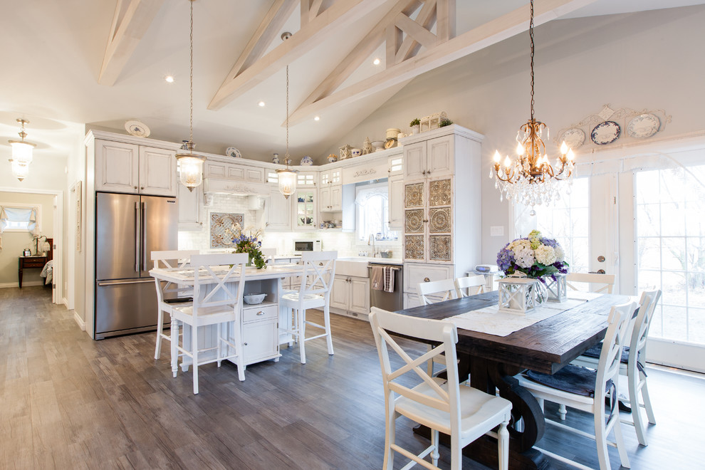 Design ideas for a mid-sized traditional l-shaped eat-in kitchen in Other with a farmhouse sink, raised-panel cabinets, distressed cabinets, white splashback, subway tile splashback, stainless steel appliances, light hardwood floors, with island and brown floor.