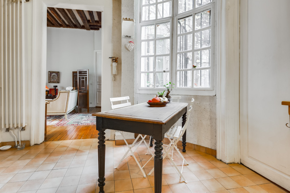 Transitional dining room in Paris with terra-cotta floors and exposed beam.
