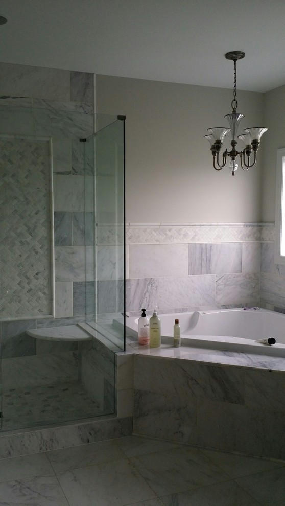 Photo of a large transitional master bathroom in Cincinnati with white tile, stone tile, grey walls, marble floors, shaker cabinets, white cabinets, a drop-in tub, a corner shower, an undermount sink, granite benchtops, a hinged shower door and grey floor.