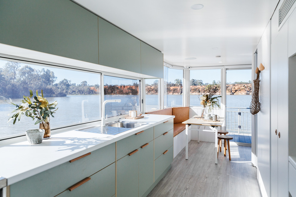 Design ideas for a beach style single-wall eat-in kitchen in Other with a drop-in sink, flat-panel cabinets, green cabinets, window splashback, panelled appliances, no island, beige floor and white benchtop.