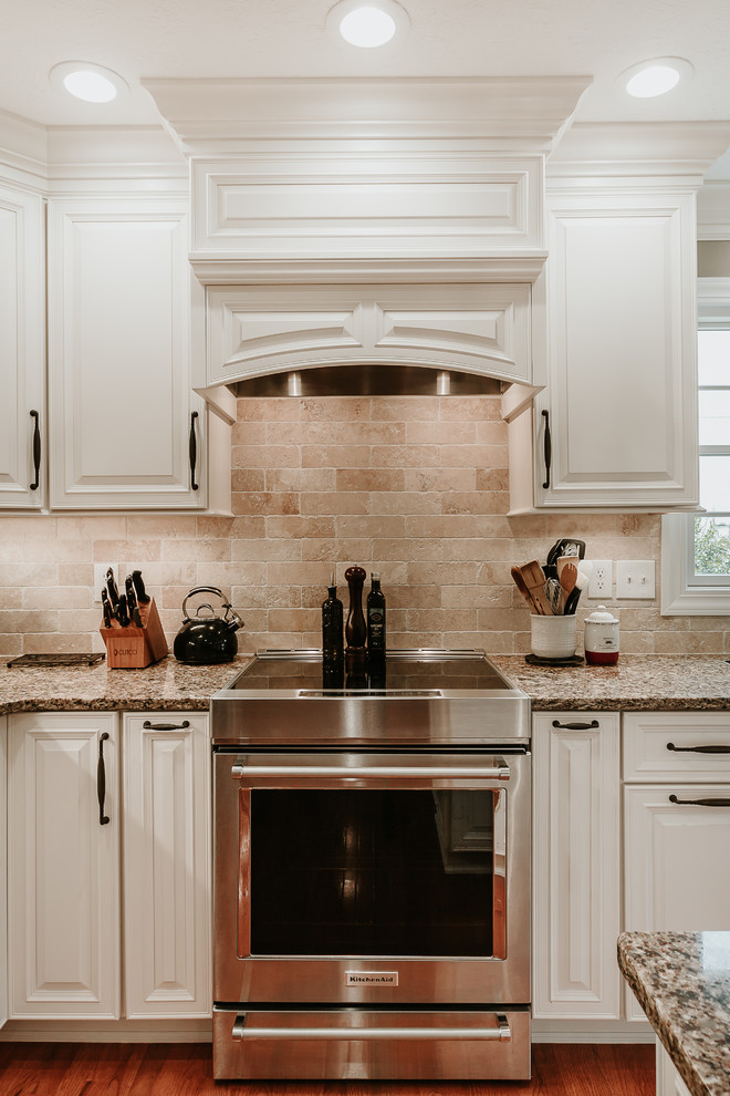 Design ideas for a mid-sized traditional l-shaped eat-in kitchen in Other with an undermount sink, raised-panel cabinets, white cabinets, granite benchtops, brown splashback, travertine splashback, stainless steel appliances, light hardwood floors, with island and brown benchtop.