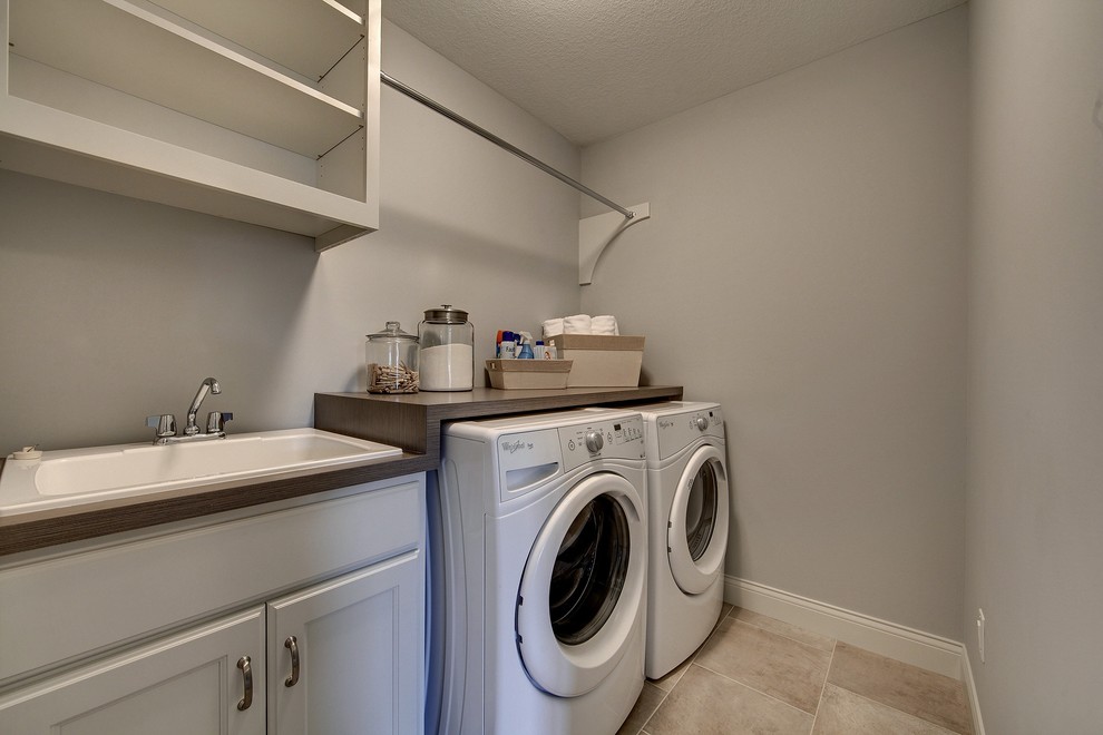 Photo of a large traditional single-wall dedicated laundry room in Minneapolis with a drop-in sink, recessed-panel cabinets, white cabinets, laminate benchtops, grey walls, ceramic floors and a side-by-side washer and dryer.