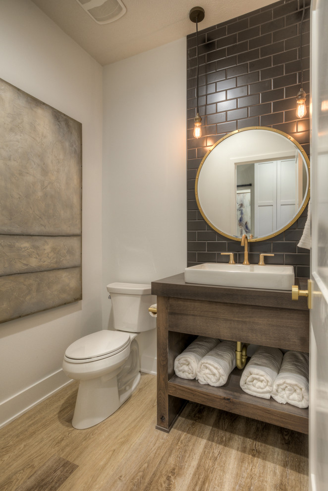 Design ideas for a country powder room in Omaha with open cabinets, dark wood cabinets, a two-piece toilet, gray tile, brown tile, subway tile, white walls, a console sink, wood benchtops, brown floor and grey benchtops.
