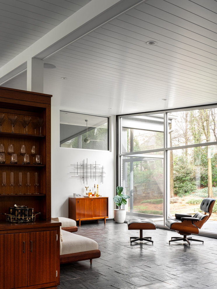 Midcentury open concept living room in Atlanta with a home bar, white walls, grey floor and slate floors.