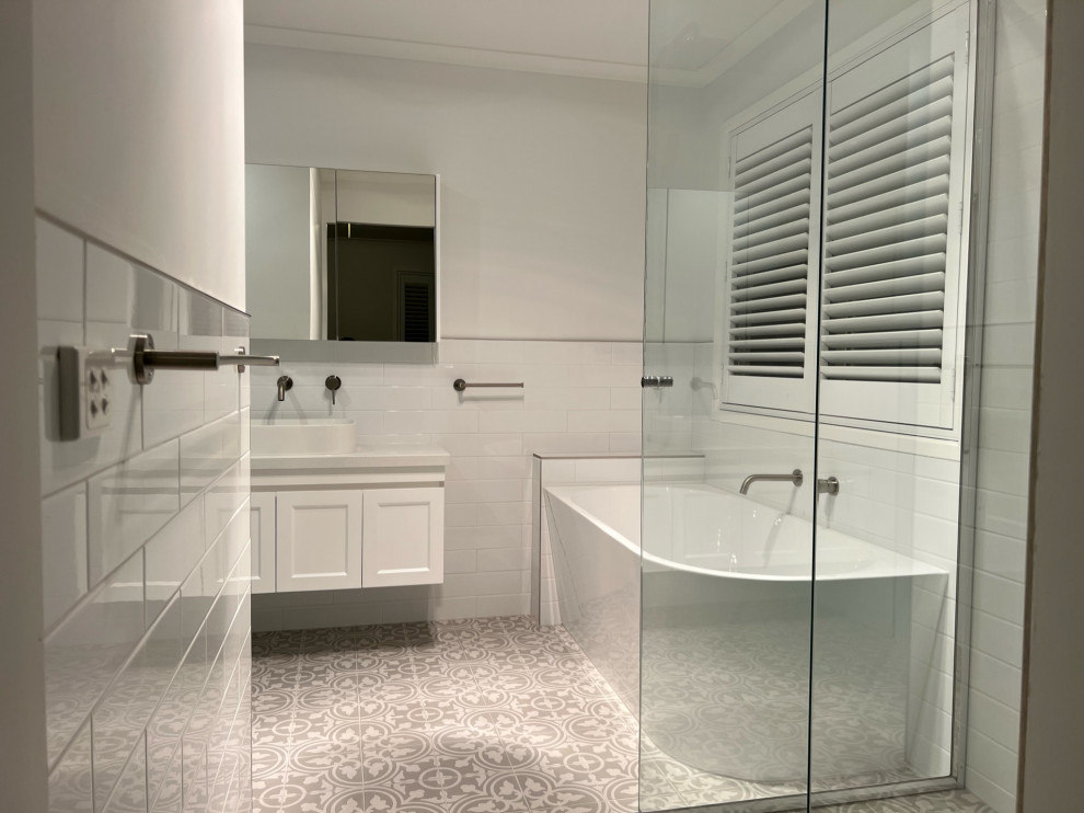 Inspiration for a mid-sized bathroom in Geelong with shaker cabinets, white cabinets, a corner tub, a wall-mount toilet, white tile, ceramic tile, ceramic floors, solid surface benchtops, multi-coloured floor, white benchtops, a single vanity and a floating vanity.
