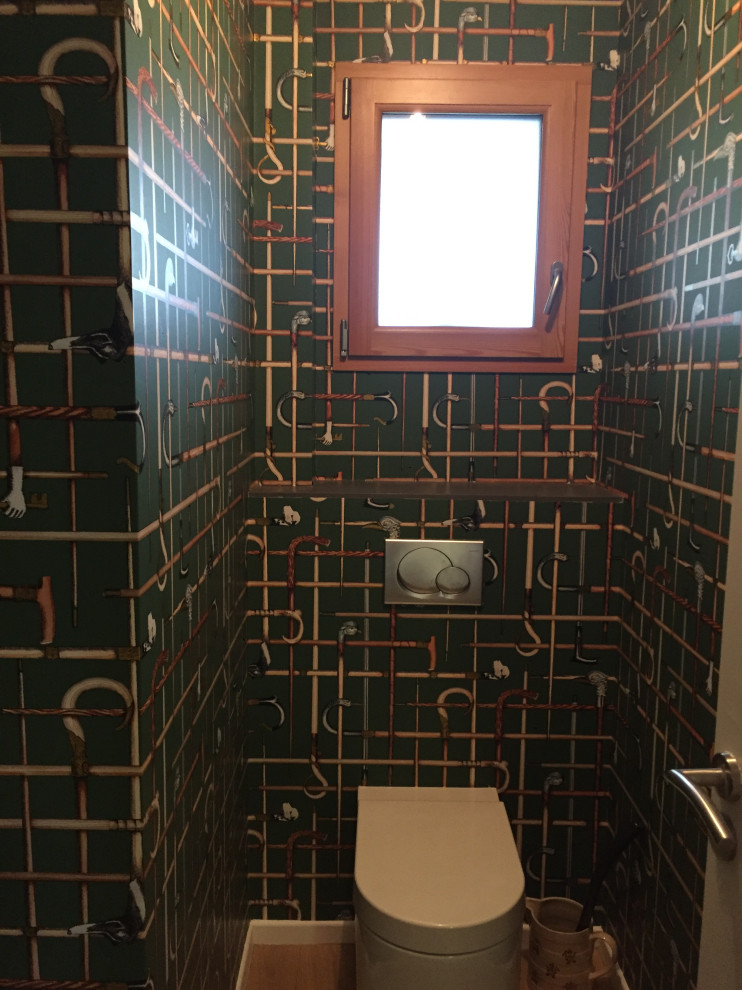 Photo of a small midcentury powder room in Other with a wall-mount toilet, green walls, light hardwood floors, a wall-mount sink and beige floor.
