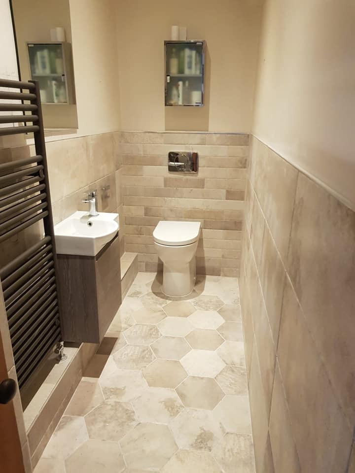 This is an example of a small traditional powder room in Manchester with flat-panel cabinets, grey cabinets, a one-piece toilet, beige tile, ceramic tile, beige walls, ceramic floors, a wall-mount sink, beige floor and a floating vanity.