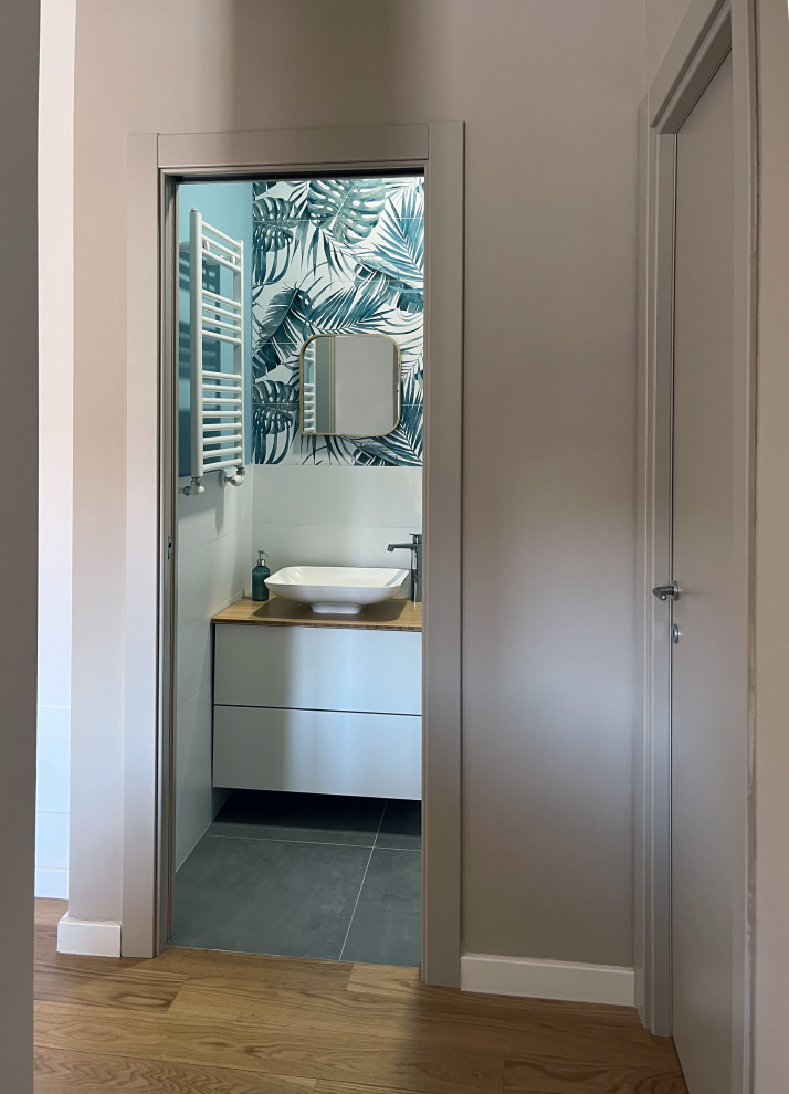 Photo of a small modern cloakroom in Rome with flat-panel cabinets, white cabinets, a one-piece toilet, multi-coloured tiles, porcelain tiles, blue walls, porcelain flooring, a vessel sink, wooden worktops, grey floors, brown worktops and a floating vanity unit.