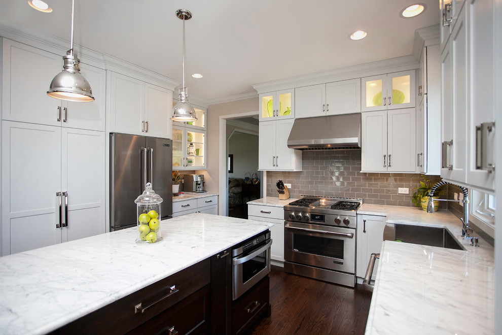 Inspiration for a large transitional l-shaped dark wood floor enclosed kitchen remodel in Chicago with a farmhouse sink, recessed-panel cabinets, white cabinets, marble countertops, beige backsplash, glass tile backsplash, stainless steel appliances and an island