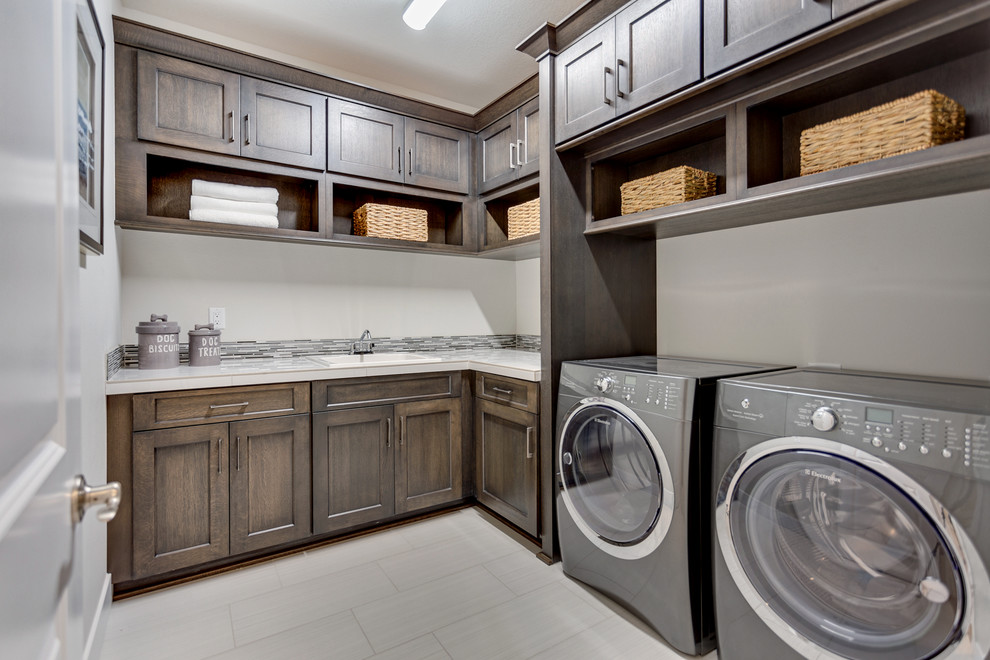 Photo of a mid-sized contemporary l-shaped dedicated laundry room in Portland with a drop-in sink, shaker cabinets, dark wood cabinets, white walls, porcelain floors, a side-by-side washer and dryer and beige floor.
