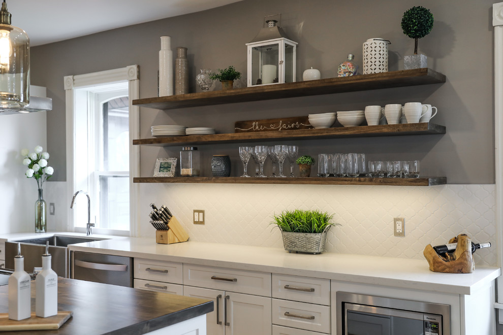 Example of a mid-sized transitional single-wall medium tone wood floor and brown floor eat-in kitchen design with a farmhouse sink, shaker cabinets, white cabinets, white backsplash, stainless steel appliances, an island and white countertops