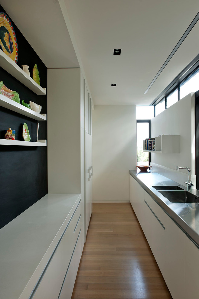 This is an example of a contemporary galley separate kitchen in Auckland with flat-panel cabinets, a double-bowl sink and stainless steel benchtops.