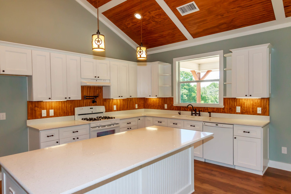 This is an example of a mid-sized country l-shaped open plan kitchen in Austin with a double-bowl sink, shaker cabinets, white cabinets, solid surface benchtops, brown splashback, timber splashback, white appliances, dark hardwood floors, with island and brown floor.