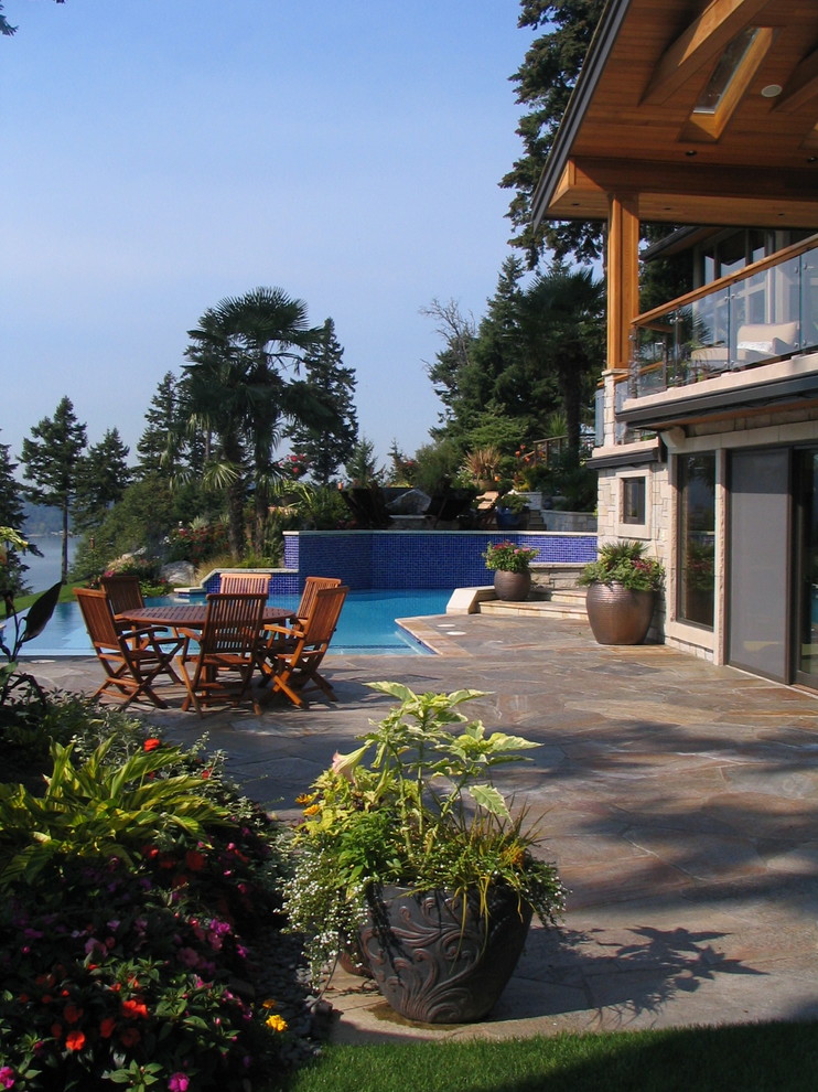 This is an example of a tropical patio in Seattle with natural stone pavers and no cover.