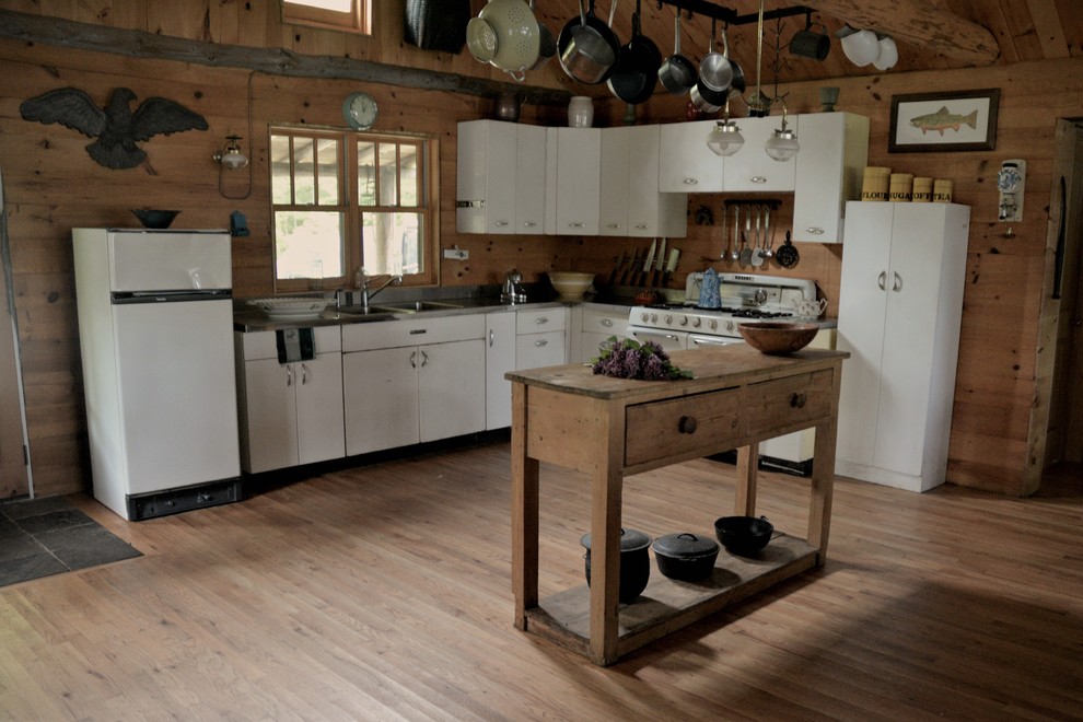 Open concept kitchen - mid-sized rustic l-shaped light wood floor open concept kitchen idea with a drop-in sink, flat-panel cabinets, white cabinets, stainless steel countertops, brown backsplash, wood backsplash, white appliances and an island