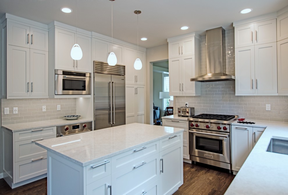 Example of a mid-sized transitional l-shaped dark wood floor and brown floor eat-in kitchen design in Seattle with a drop-in sink, shaker cabinets, white cabinets, quartz countertops, white backsplash, ceramic backsplash, stainless steel appliances, an island and white countertops