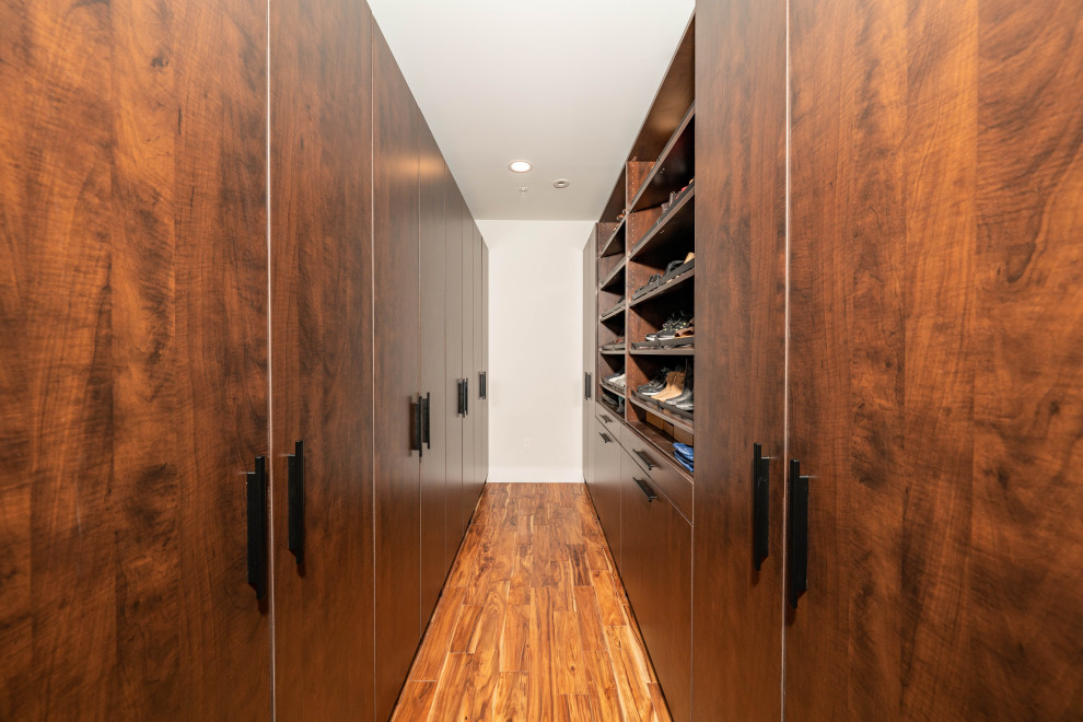 Cette image montre une grande armoire encastrée minimaliste en bois foncé avec un placard à porte plane, parquet clair et un sol marron.