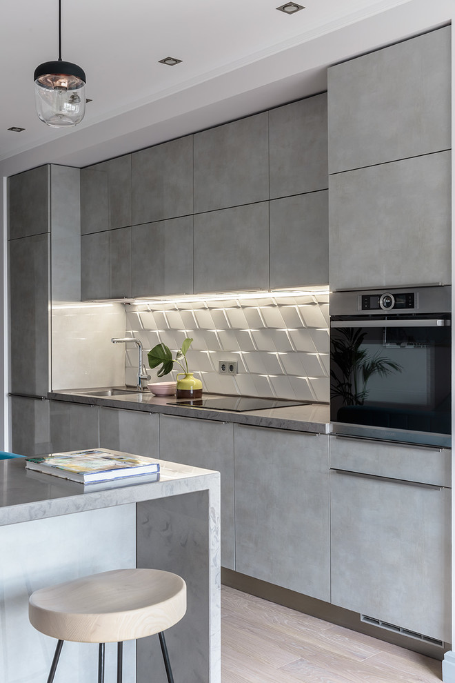 Inspiration for a mid-sized contemporary single-wall kitchen in Saint Petersburg with white splashback, ceramic splashback, light hardwood floors, with island, grey benchtop, flat-panel cabinets, grey cabinets, stainless steel appliances, beige floor and a single-bowl sink.