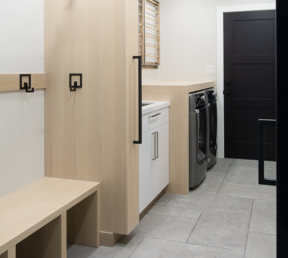 Photo of a mid-sized modern single-wall utility room in San Francisco with an undermount sink, flat-panel cabinets, light wood cabinets, wood benchtops, grey walls, limestone floors, a side-by-side washer and dryer, grey floor and brown benchtop.