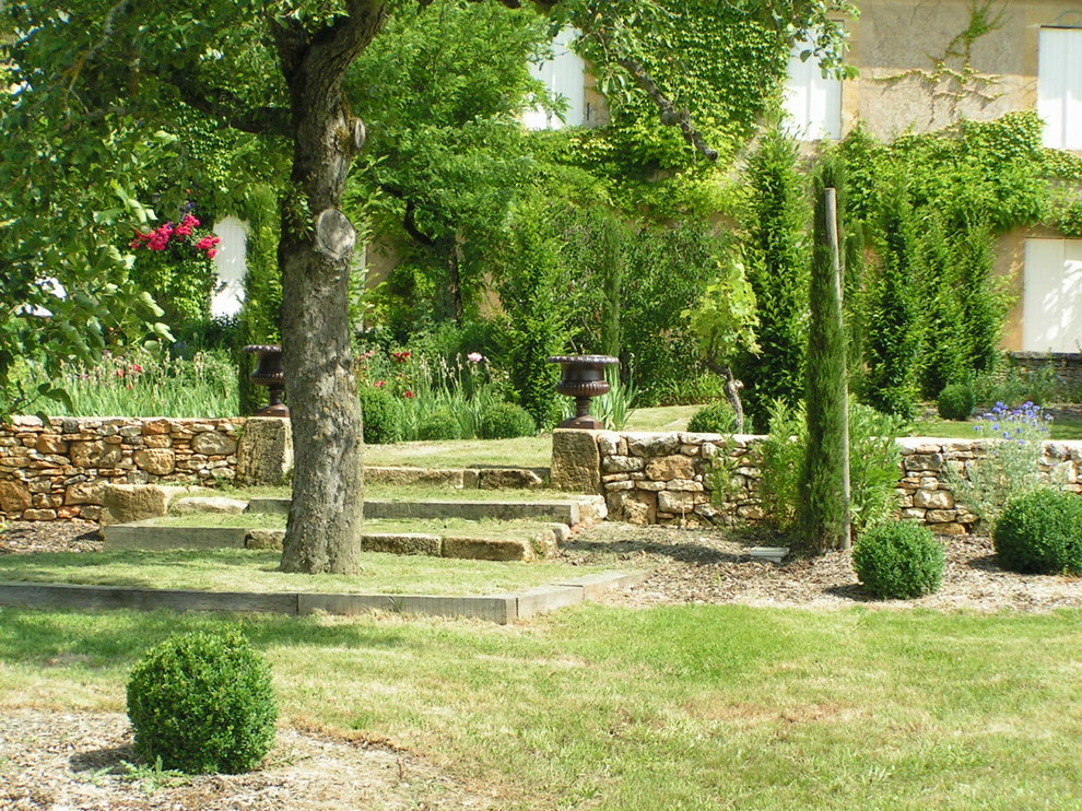 Large traditional shaded formal garden in Bordeaux with natural stone pavers for summer.