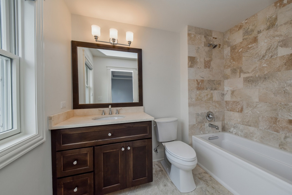This is an example of a mid-sized country kids bathroom in Chicago with recessed-panel cabinets, dark wood cabinets, an alcove tub, an alcove shower, a two-piece toilet, beige tile, porcelain tile, white walls, porcelain floors, an undermount sink, engineered quartz benchtops, beige floor, a shower curtain, beige benchtops, a shower seat, a single vanity and a built-in vanity.
