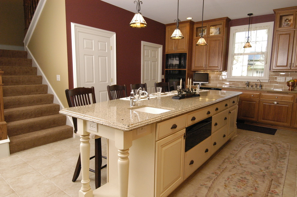 This is an example of a traditional l-shaped eat-in kitchen in Milwaukee with an undermount sink, raised-panel cabinets, medium wood cabinets, quartz benchtops, brown splashback, glass tile splashback and black appliances.