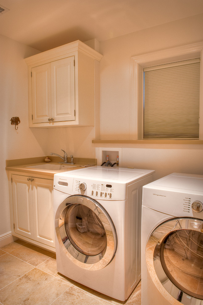 Photo of a mid-sized beach style single-wall utility room with a drop-in sink, beaded inset cabinets, white cabinets, white walls and a side-by-side washer and dryer.