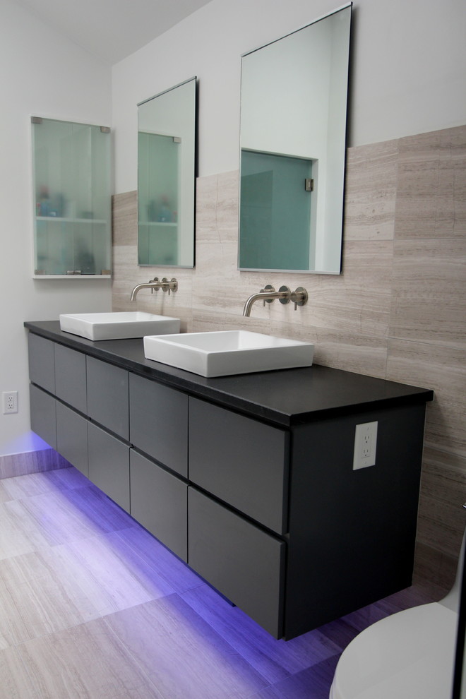 Photo of a mid-sized contemporary master bathroom in Atlanta with a vessel sink, grey cabinets, gray tile, flat-panel cabinets, a freestanding tub, a curbless shower, a two-piece toilet, stone tile, white walls, limestone floors, granite benchtops, grey floor, an open shower, black benchtops, a niche, a double vanity, a floating vanity and vaulted.