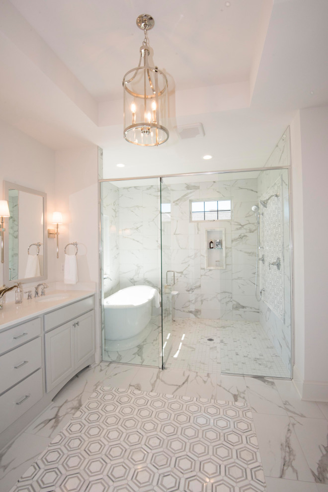 This is an example of a large transitional master wet room bathroom in Milwaukee with grey cabinets, a freestanding tub, a two-piece toilet, gray tile, marble, white walls, marble floors, an undermount sink, engineered quartz benchtops, grey floor, a hinged shower door, white benchtops and recessed-panel cabinets.