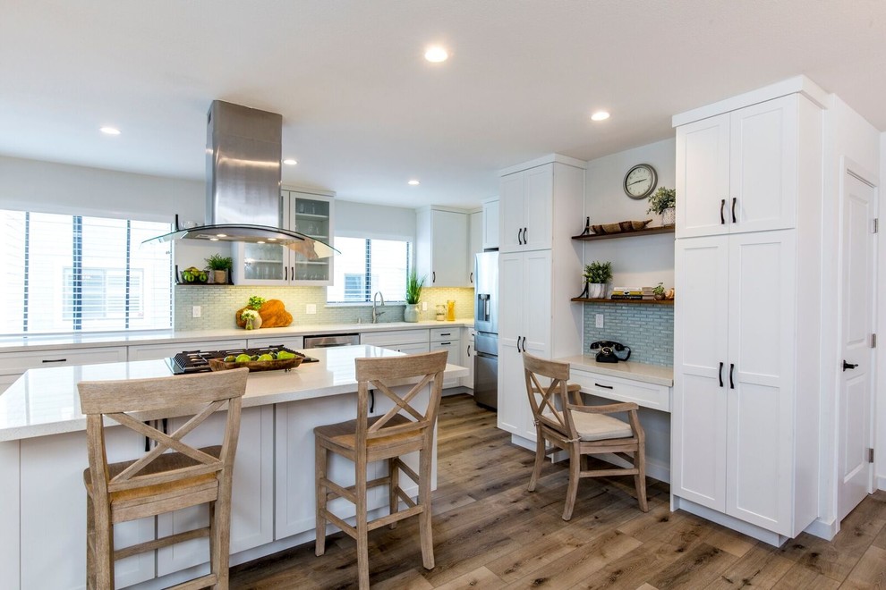 This is an example of a mid-sized transitional l-shaped open plan kitchen in Los Angeles with shaker cabinets, white cabinets, quartz benchtops, with island, white benchtop, an undermount sink, blue splashback, glass tile splashback, stainless steel appliances, medium hardwood floors and brown floor.