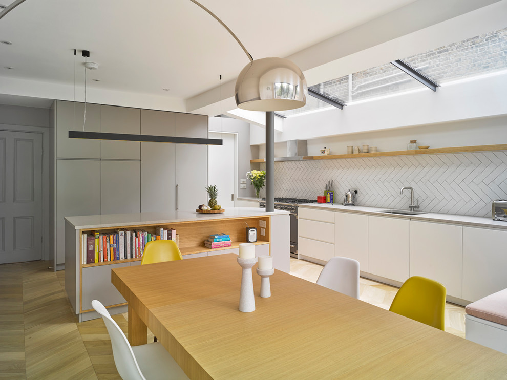 Inspiration for a mid-sized contemporary single-wall eat-in kitchen in London with an undermount sink, flat-panel cabinets, white cabinets, white splashback, subway tile splashback, panelled appliances, light hardwood floors, with island and beige floor.