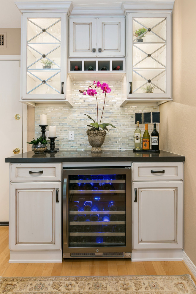 This is an example of a small transitional single-wall home bar in San Diego with raised-panel cabinets, quartz benchtops, white splashback, glass tile splashback and beige cabinets.