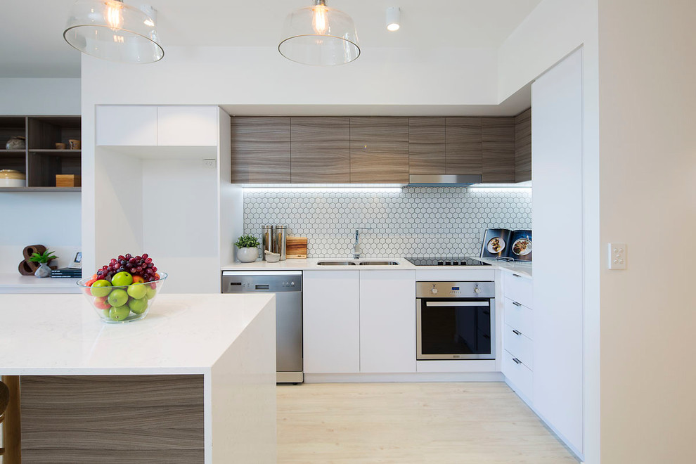 Contemporary l-shaped kitchen in Brisbane with a double-bowl sink, flat-panel cabinets, medium wood cabinets, white splashback, mosaic tile splashback, stainless steel appliances, light hardwood floors, with island, beige floor and white benchtop.