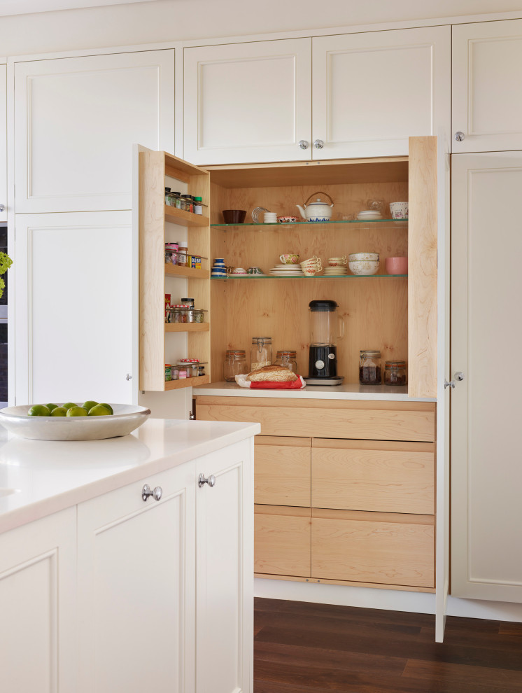 This is an example of a large traditional l-shaped eat-in kitchen in London with an integrated sink, recessed-panel cabinets, white cabinets, solid surface benchtops, yellow splashback, panelled appliances, dark hardwood floors, with island, brown floor and white benchtop.