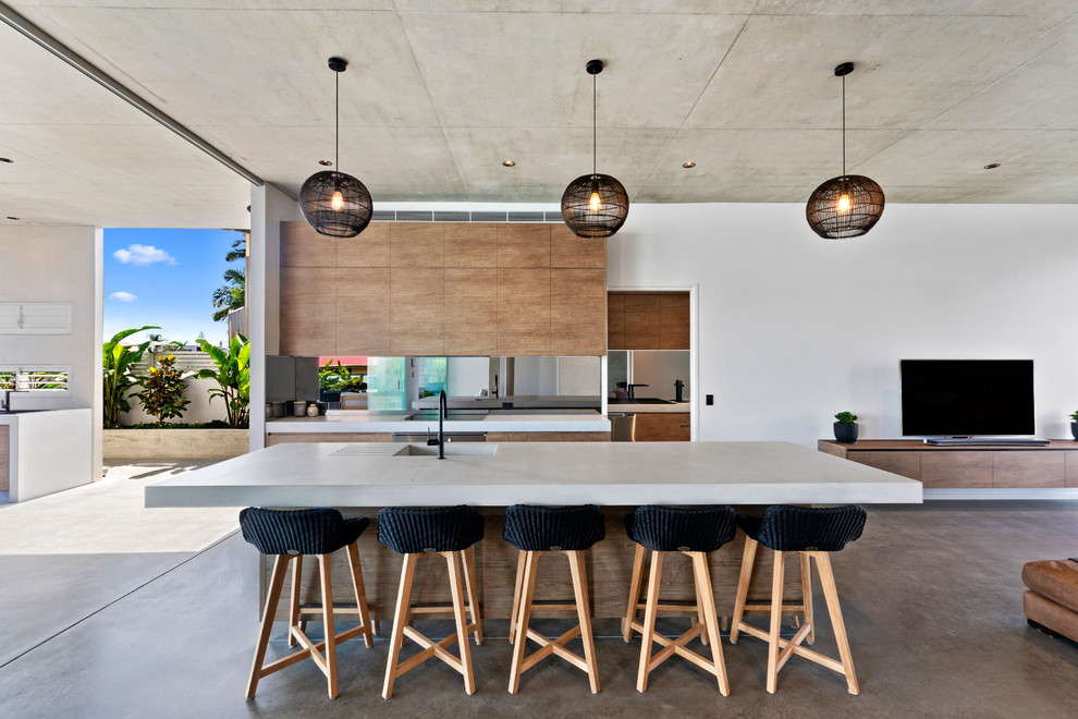 Contemporary galley open plan kitchen in Sunshine Coast with an integrated sink, flat-panel cabinets, medium wood cabinets, window splashback, stainless steel appliances, concrete floors, with island, brown floor and white benchtop.