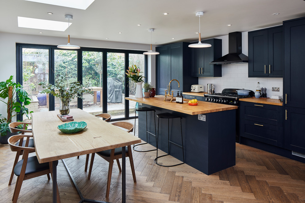 Design ideas for a contemporary galley eat-in kitchen in London with an undermount sink, shaker cabinets, black cabinets, wood benchtops, white splashback, subway tile splashback, panelled appliances, medium hardwood floors, with island, brown floor and brown benchtop.