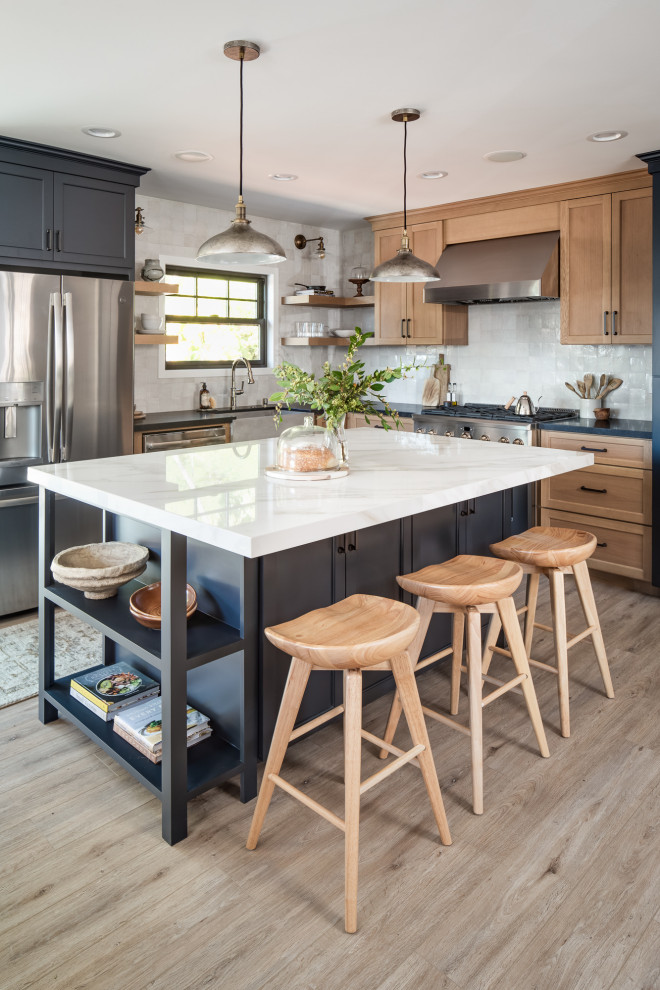 Inspiration for a mid-sized transitional l-shaped eat-in kitchen in San Diego with a farmhouse sink, shaker cabinets, blue cabinets, solid surface benchtops, white splashback, terra-cotta splashback, black appliances, vinyl floors, with island, beige floor and black benchtop.