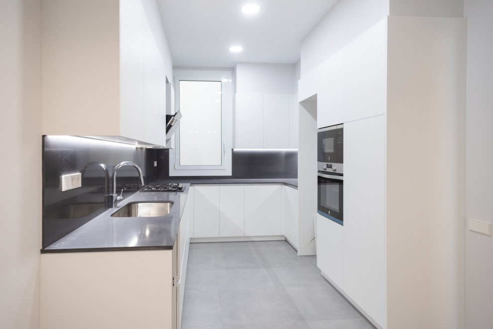 Design ideas for a medium sized mediterranean u-shaped enclosed kitchen in Barcelona with a single-bowl sink, flat-panel cabinets, white cabinets, black splashback, stainless steel appliances, ceramic flooring, no island, grey floors and black worktops.
