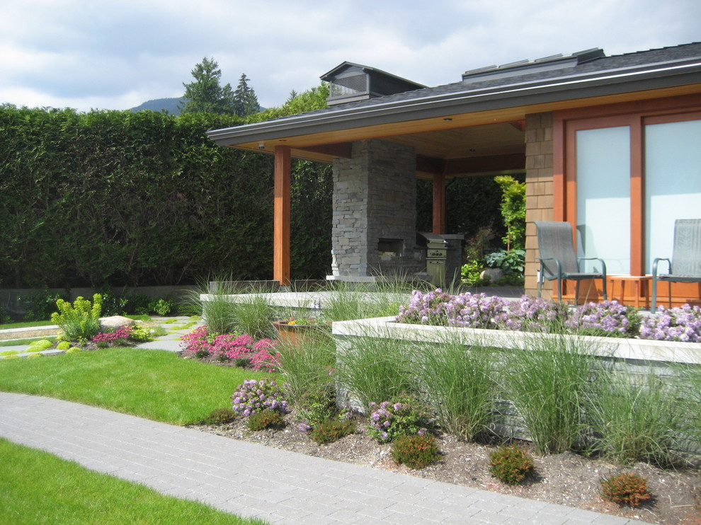 This is an example of a large contemporary front yard full sun driveway in Vancouver with a retaining wall and natural stone pavers.