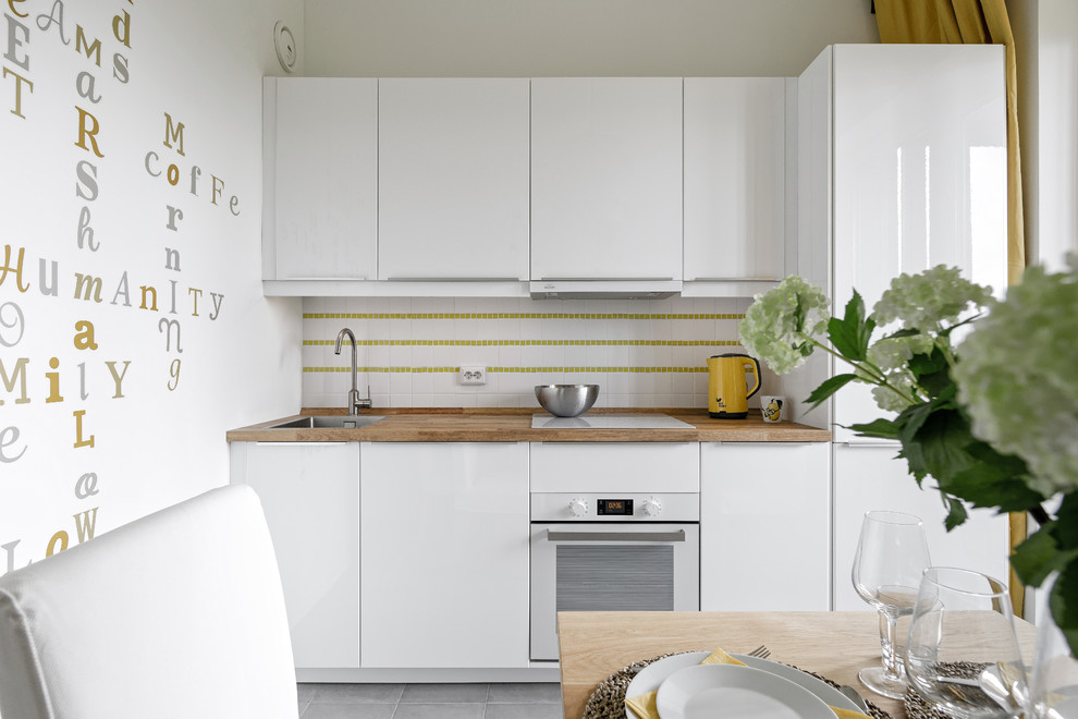 Small scandinavian single-wall separate kitchen in Saint Petersburg with a drop-in sink, flat-panel cabinets, white cabinets, wood benchtops, white splashback, white appliances, no island, grey floor and brown benchtop.