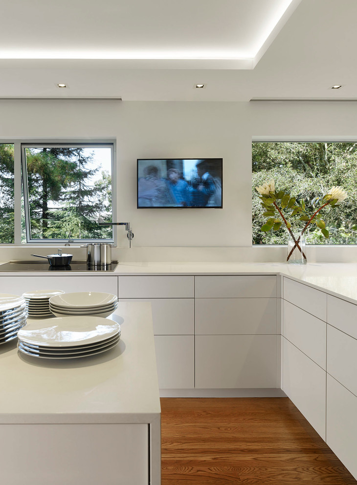 Design ideas for a large modern u-shaped eat-in kitchen in San Francisco with an undermount sink, flat-panel cabinets, white cabinets, white splashback, panelled appliances, medium hardwood floors, with island and solid surface benchtops.