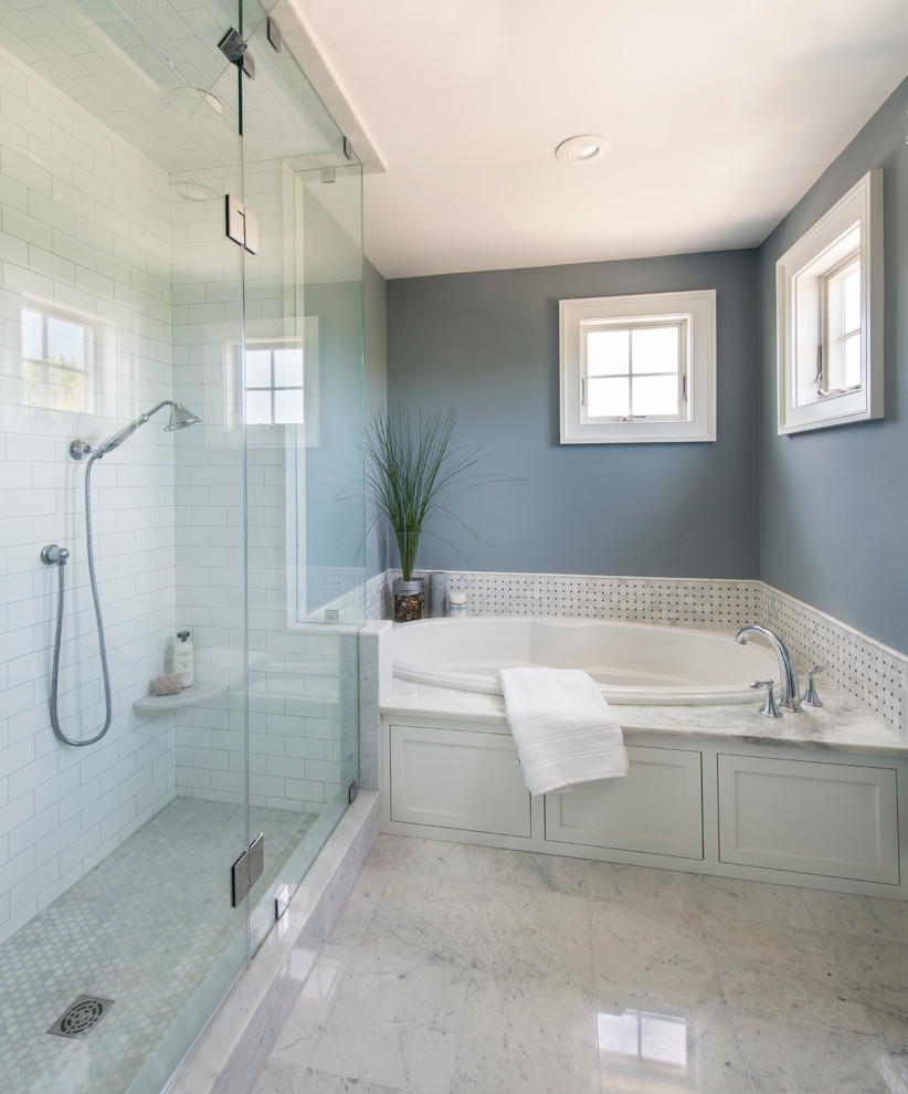 This is an example of a mid-sized beach style bathroom in Providence with beaded inset cabinets, white cabinets, a drop-in tub, a two-piece toilet, white tile, stone tile, grey walls, marble floors, an undermount sink and marble benchtops.